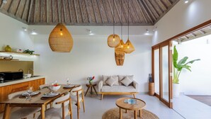 Ein modernes Wohnzimmer mit Essbereich, ausgestattet mit Holzboden, gewebten Pendelleuchten, einem Sofa und einem Couchtisch.