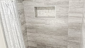 A shower with a rain showerhead, a shower curtain with text, and a hexagonal tile pattern on the floor.
