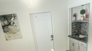 A bedroom with a bed, a door, a small kitchenette, and a bathroom. - Cozy and Charming Studio in Fort Lauderdale (Fort Lauderdale)