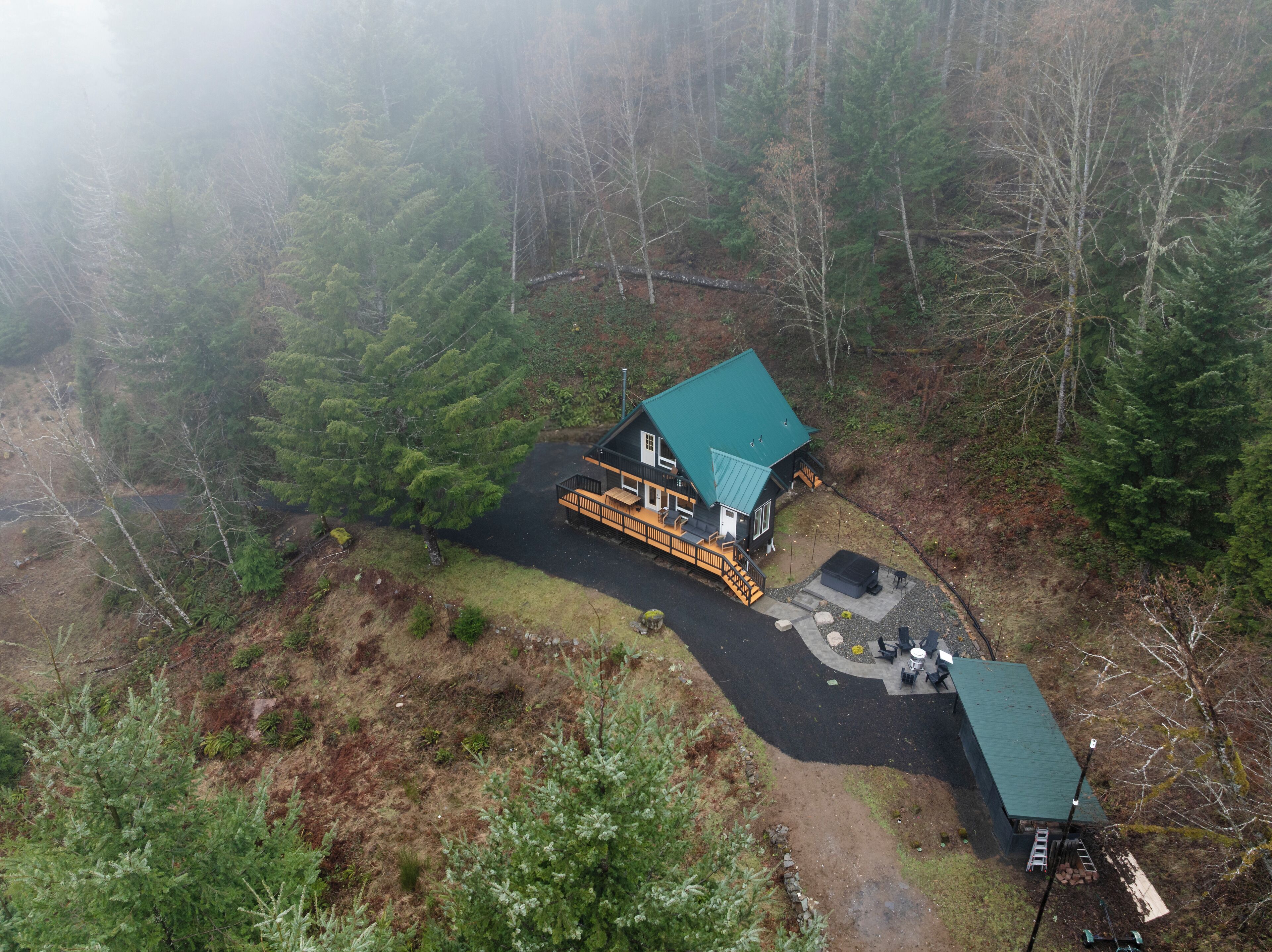 An aerial view of a cabin with a green roof, surrounded by dense forest.
