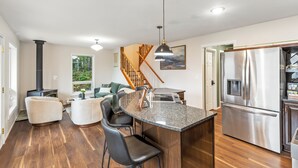 A modern kitchen with a central island, stainless steel appliances, and a wooden staircase. - The Peak: Hot tub + Mt. Views (Packwood)