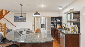 A modern kitchen with a granite countertop, stainless steel appliances, and a wooden staircase. - The Peak: Hot tub + Mt. Views (Packwood)
