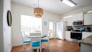 A bright kitchen with white cabinets, a microwave, and a stove. There is a dining table with blue chairs.