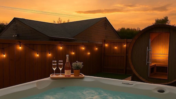 Un jacuzzi con terraza de madera y luces colgantes, una cabaña de madera y una valla de madera.