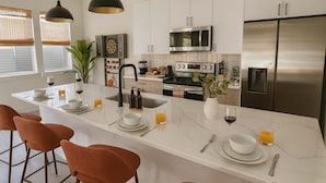Una cocina moderna con una isla central, electrodomésticos de acero inoxidable e iluminación colgante.