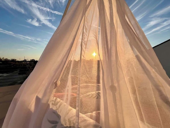 A tent-like structure with a sheer fabric, possibly a canopy or tent, set against a clear sky with the sun visible through the gaps.