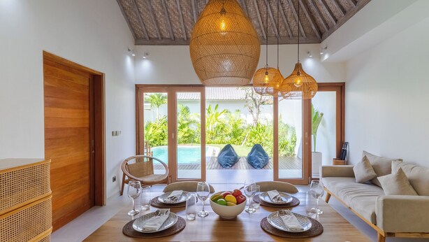 A dining area with a wooden table set for four, a bowl of fruit, and a sofa in the background. - Villa Sylvia by Pertama Stay (Kerobokan)