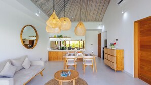 A modern living room with a sofa, dining table, and chairs, a kitchen in the background, and a large mirror on the wall. - Villa Sylvia by Pertama Stay (Kerobokan)