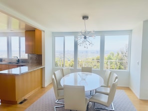 Uma cozinha moderna com uma ilha grande, uma área de jantar com mesa redonda e cadeiras, e janelas amplas com vista para a cidade.