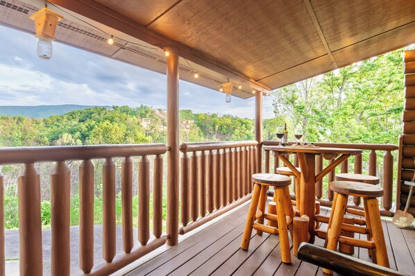 A wooden deck with a railing, wooden stools, and a table with wine glasses.