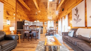 A wooden cabin interior with a living room, dining area, and kitchen.