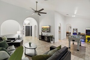 A spacious living area with a sofa, coffee table, and a foosball table. There is a television mounted on the wall and a door leading to another room. - Mesa Luxury Home. Hot tub, Pool, Golf, Basketball Court and MORE (Mesa)