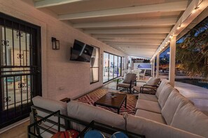 An indoor/outdoor living area with a pool, seating, and a TV.