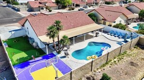 A residential area with a swimming pool, a covered patio, and a basketball court.