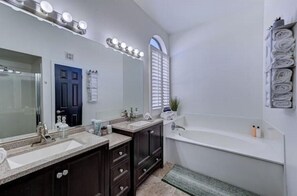 A modern bathroom with a large mirror, vanity with two sinks, a bathtub, and a towel rack.