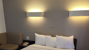 Ett hotellrum med en säng, en stol, ett sängbord med en telefon och två väggmonterade lampor.