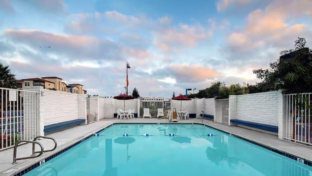 En rektangulär swimmingpool med en vit kakelbeklädd poolkant, omgiven av vita väggar och metallgrindar.