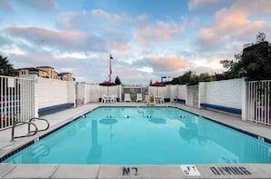 Piscina rectangular con borde de baldosas blancas, rodeada por muros blancos y portones de metal.