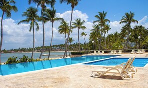A pool with lounge chairs, palm trees, and a beach in the background. - Nueva Romana Beach: 3 bedrooms + 10 guests + pool + golf + tennis + beach (Playa nueva romana)