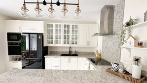 A modern kitchen with white cabinets, a granite countertop, a built-in oven, a stove, and a hanging light fixture.