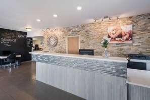 Zona de recepción de un hotel con pared de piedra, un reloj, una máquina de café y un escritorio con un ordenador.
