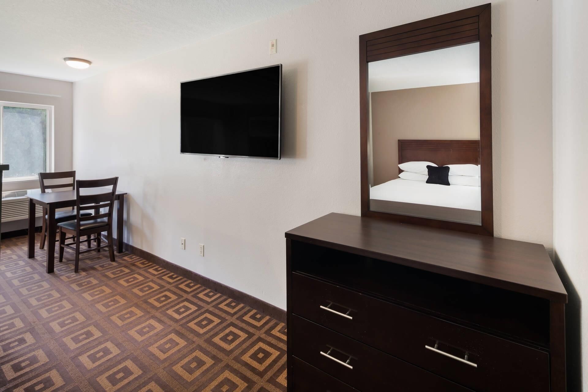 Habitació d'hotel amb un llit, un televisor penjat a la paret, una petita arca i una cadira.