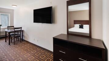 Habitació d'hotel amb un llit, un televisor penjat a la paret, una petita arca i una cadira.