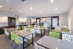A modern dining area with multiple tables and chairs, a kitchen area with a coffee machine, and a counter with a menu board. - Quality Inn & Suites Kennewick Tri-Cities (Kennewick)