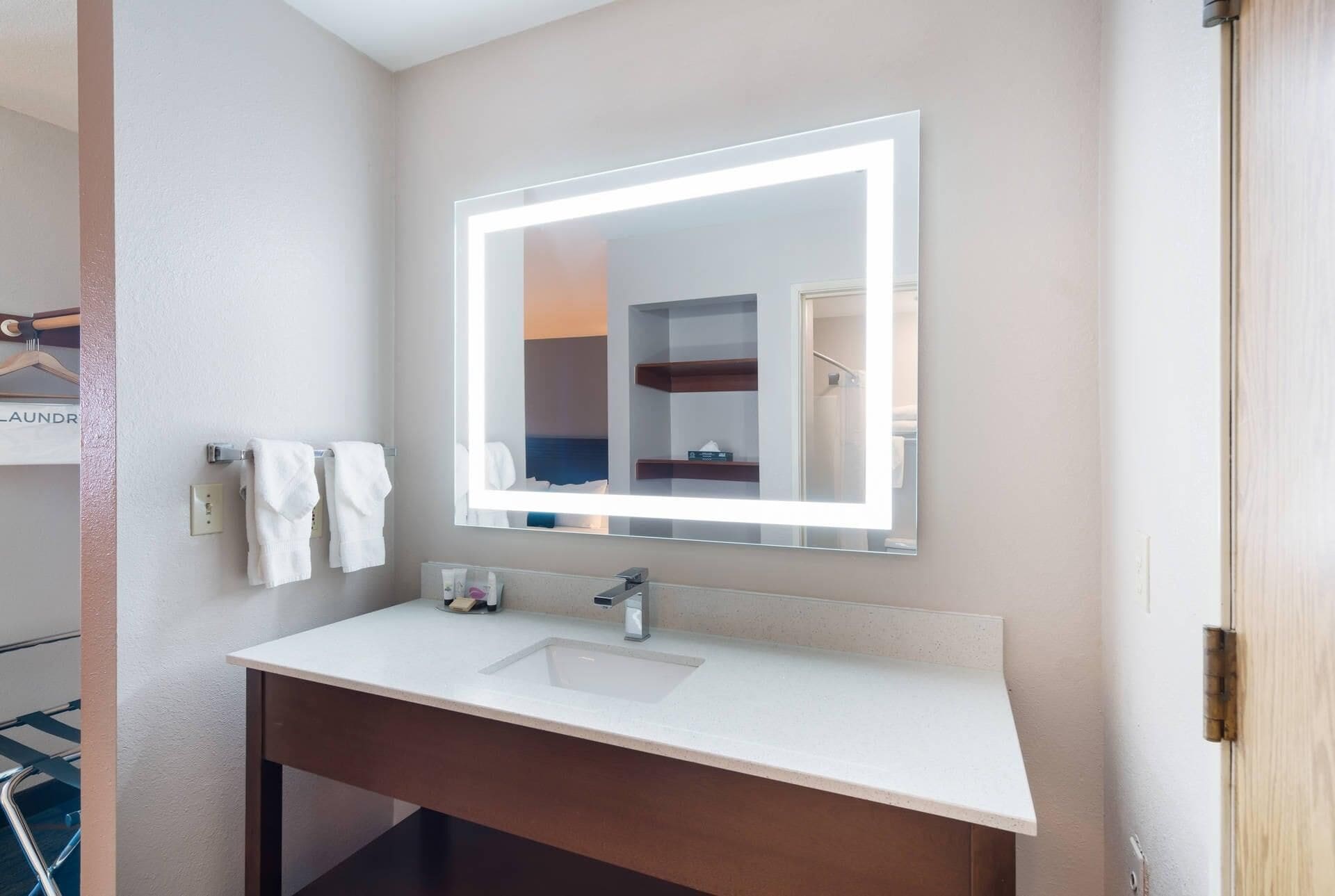 A bathroom with a white sink, a mirror with a light, and a towel rack.
