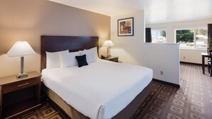 Una habitación de hotel con una cama grande, dos mesitas de noche con lámparas, un escritorio pequeño y una ventana con vistas al exterior.