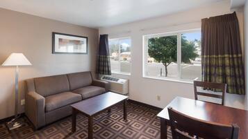 A hotel room with a sofa, a small table, a chair, a lamp, and a window with curtains.