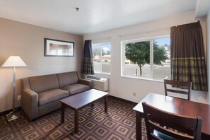 A hotel room with a sofa, a small table, a chair, a lamp, and a window with curtains. - Quality Inn & Suites Kennewick Tri-Cities (Kennewick)