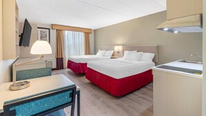 A hotel room with two beds, a desk, a chair, a lamp, a TV, a window with curtains, and a kitchenette. - MainStay Suites Lansing West (Lansing)