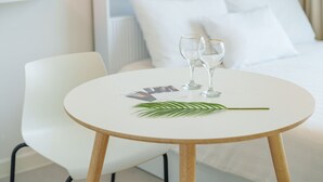 A neatly arranged hotel room with a white bed, a white chair, a small round table with two wine glasses and a leaf, and a calendar. - Yangyang Sunrise Sea Pension (Yangyang)