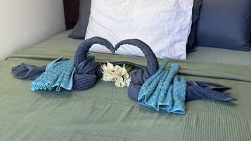 A neatly made bed with a green bedspread, two heart-shaped towels, and a small bouquet of flowers.