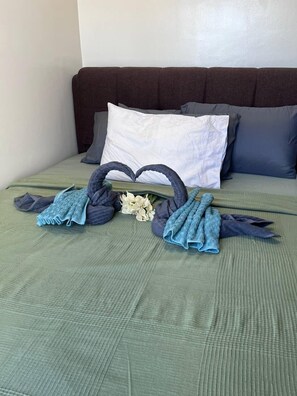A neatly made bed with a green bedspread, two heart-shaped towels, and a small bouquet of flowers. - BAYSHORE RESIDENTIAL RESORT 2 PHASE 1 (Parañaque)