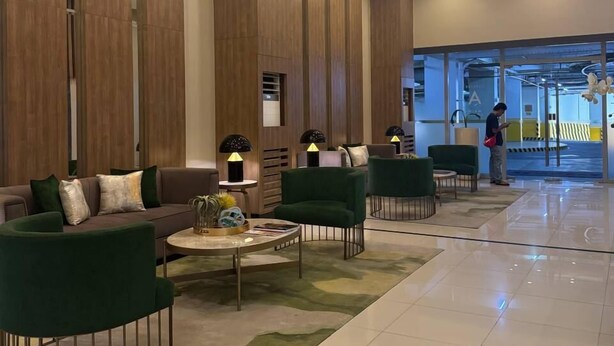 A modern lobby with a reception desk, green seating area, and a large window. - BAYSHORE RESIDENTIAL RESORT 2 PHASE 1 (Parañaque)