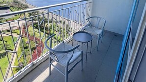 A balcony with two chairs and a small table, overlooking a landscaped area and a body of water. - BAYSHORE RESIDENTIAL RESORT 2 PHASE 1 (Parañaque)