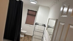 Un baño con inodoro, ventana con persiana, toallero y cortina de ducha.