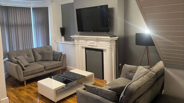 Una sala de estar con un sofá gris, una mesa de centro blanca, una chimenea y un televisor de pantalla plana montado encima.
