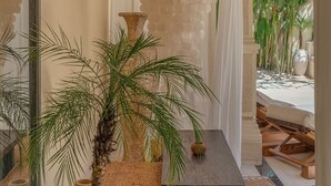 A corridor with a palm tree, a stone vase, and a woven bench.
