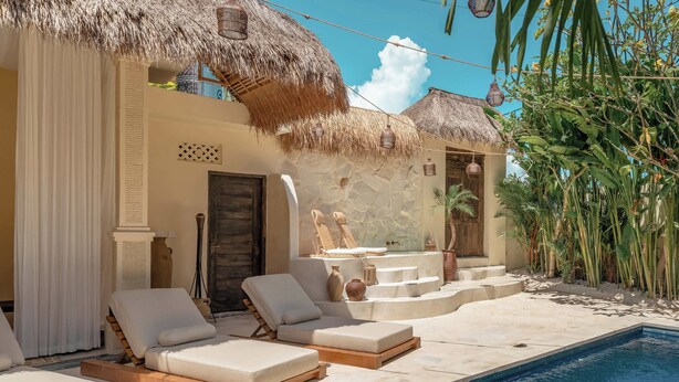 A poolside area with lounge chairs, a thatched-roof structure, and a stone wall.