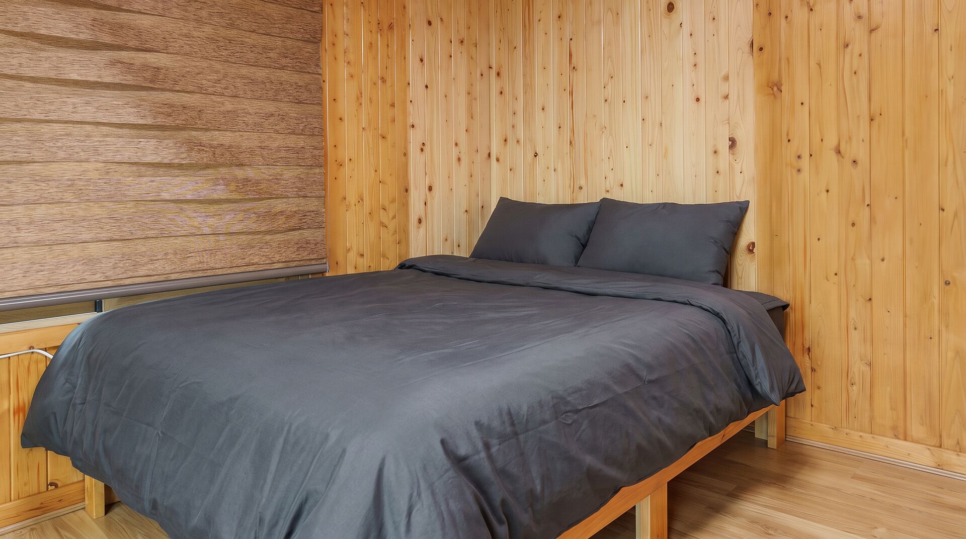 Ein Einzelbett mit dunkelbrauner Matratze und Kissen, vor einer Wand aus vertikalen Holzplanken.