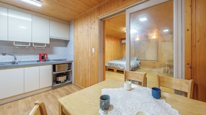 A compact kitchen with modern appliances, a dining area with a table and chairs, and a bedroom visible through a glass door. - Gyeongju Happy Dream Ocean View Pension (Gyeongju)