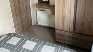 Une chambre à coucher de taille modeste, avec une armoire en bois, un radiateur et un lit recouvert d’une couette à carreaux.