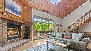 Ein gemütliches Wohnzimmer mit Kamin, großem Fenster, einer Treppe und einem modernen Sofa.