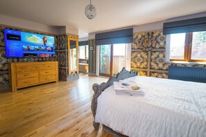 Une chambre avec un grand lit, une commode en bois, un téléviseur et un mur décoré d’un motif.
