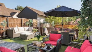 A patio with wicker furniture, a table with bowls and a plant, and a wooden fence. - Sampford Hideaway Retreat (Little Sampford)