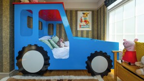 A child's bed designed like a blue truck with large wheels, stuffed animals, and a Mickey Mouse pillow. - Sampford Hideaway Retreat (Little Sampford)