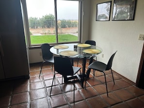 Un comedor con una mesa de vidrio, cuatro sillas y dos individuales tejidos.